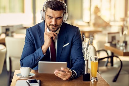 businessman-wearing-headphones-while-surfing-net-touchpad-cafe